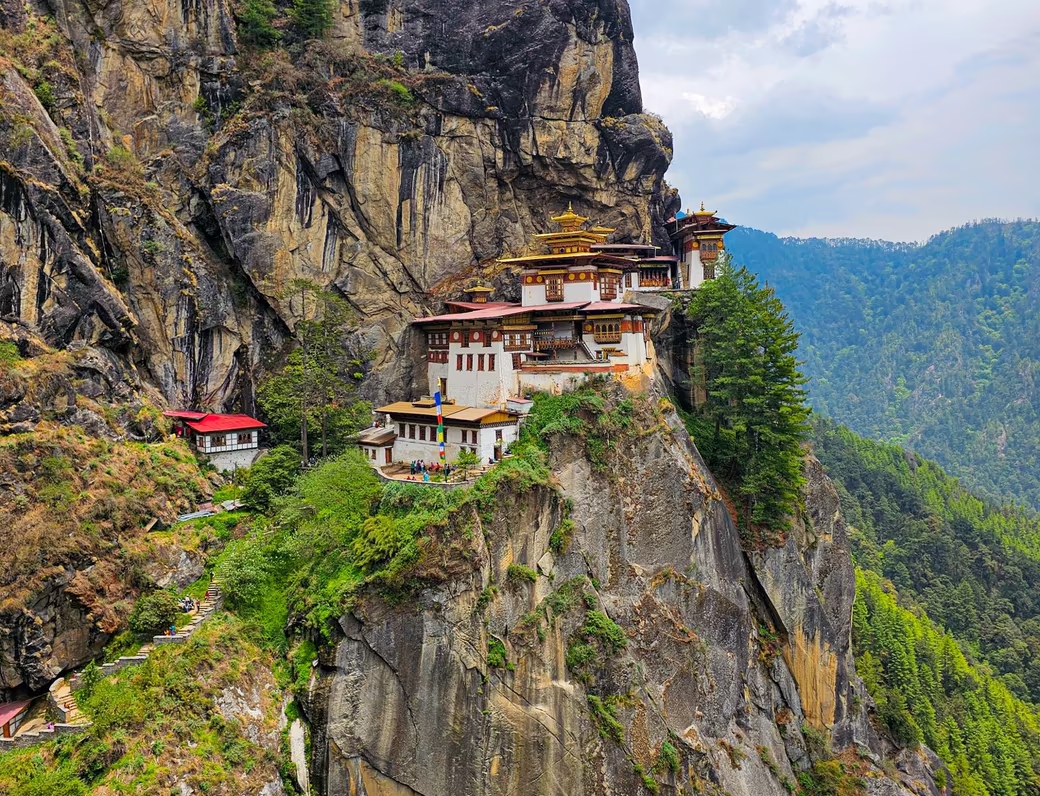 A portrait view of Tiger’s Nest Monastery clinging to a forested cliff in Bhutan